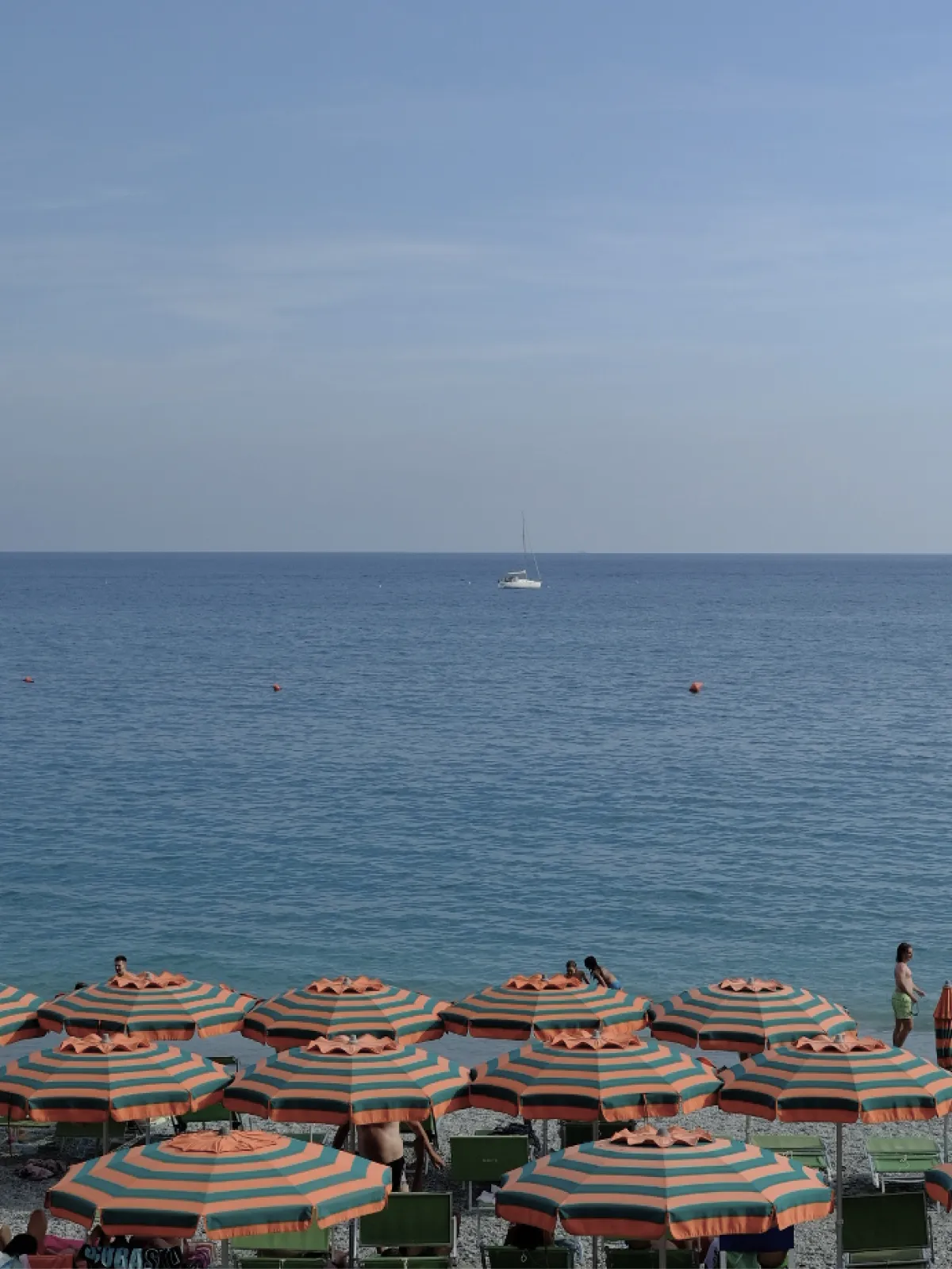 Striped beach umbrellas along a shoreline with a sailboat on the horizon.