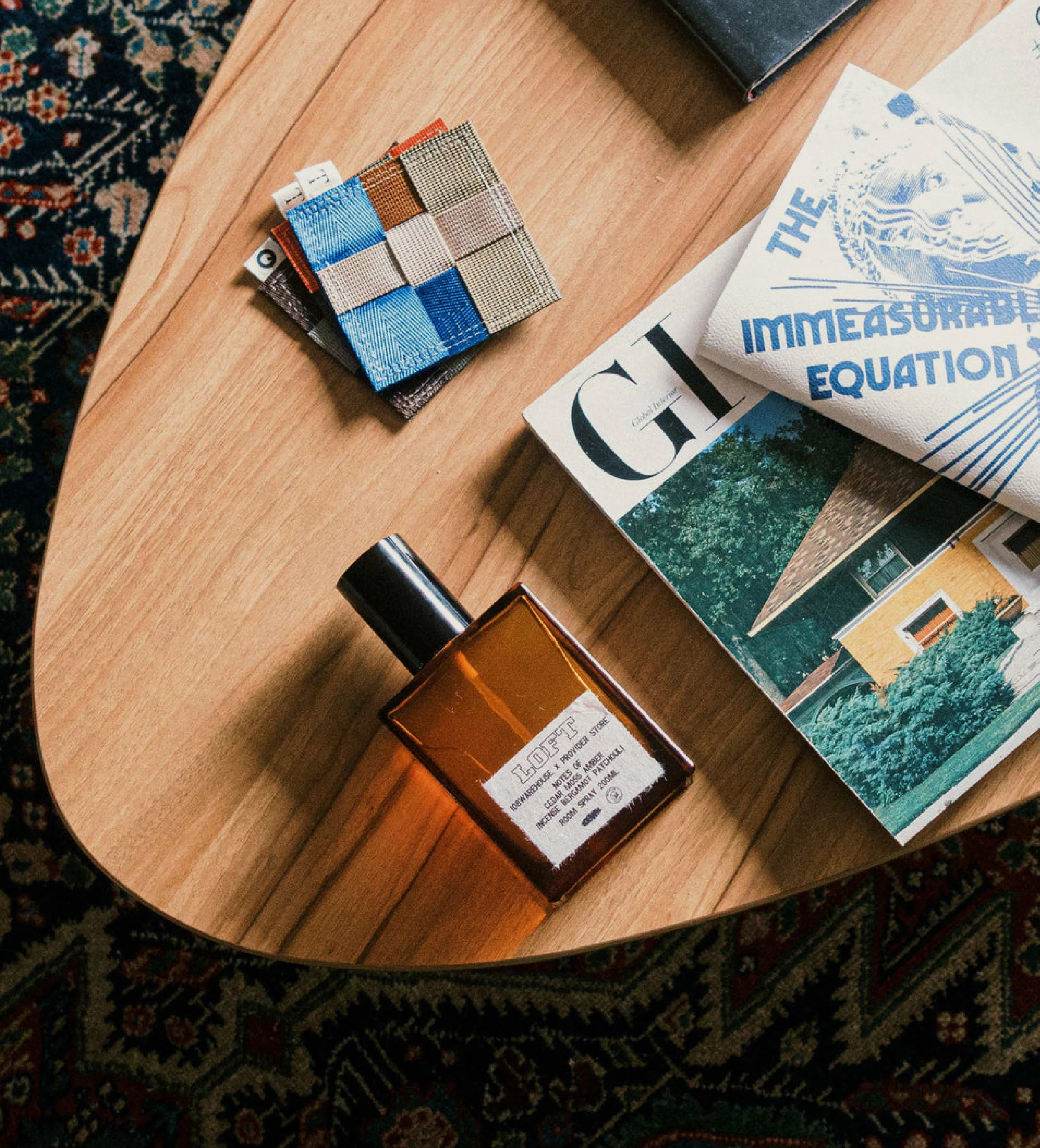 A room spray bottle, fabric swatches, and magazines styled on a wooden table.