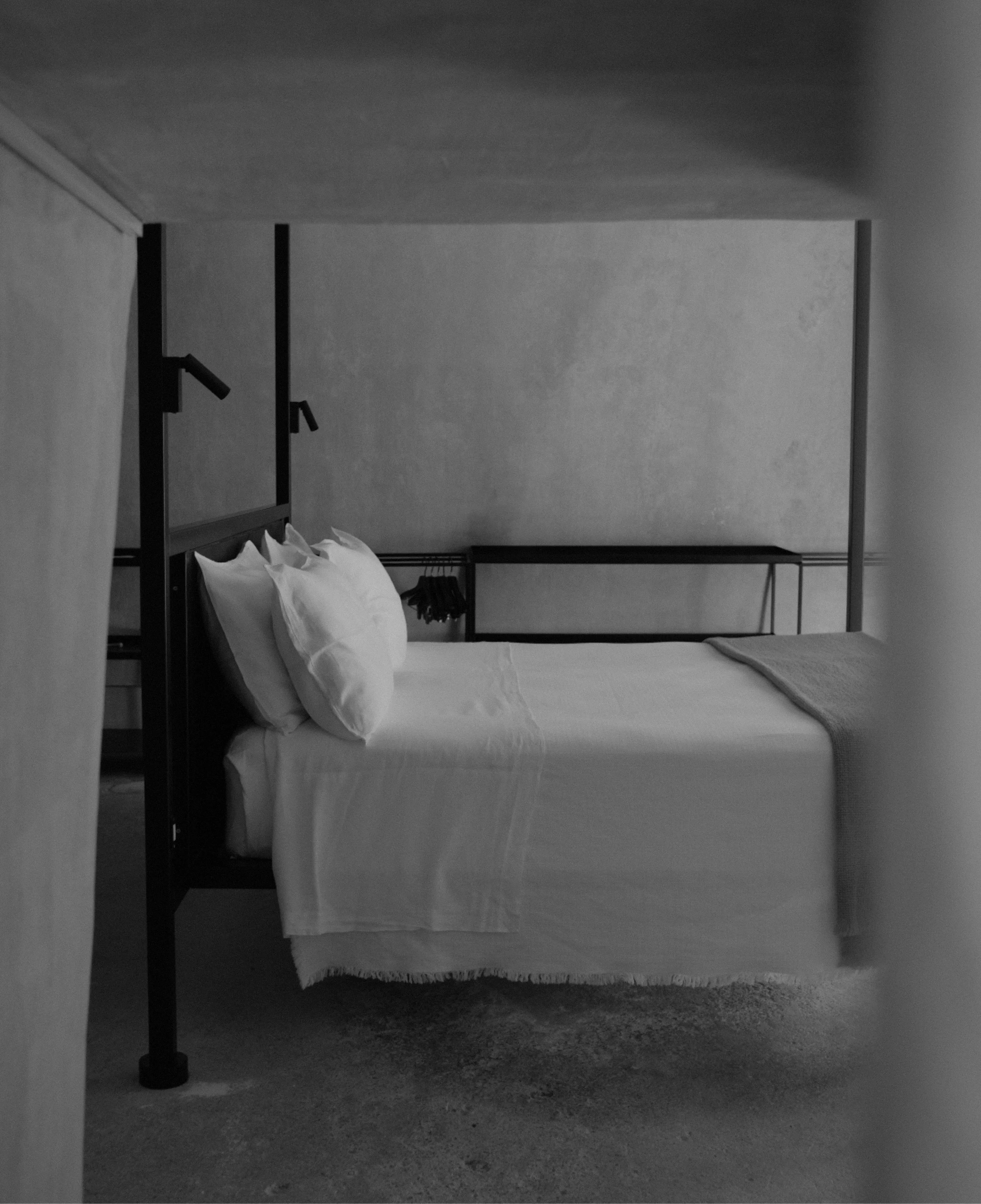 A minimal bedroom with a dark metal bed frame and plaster walls.